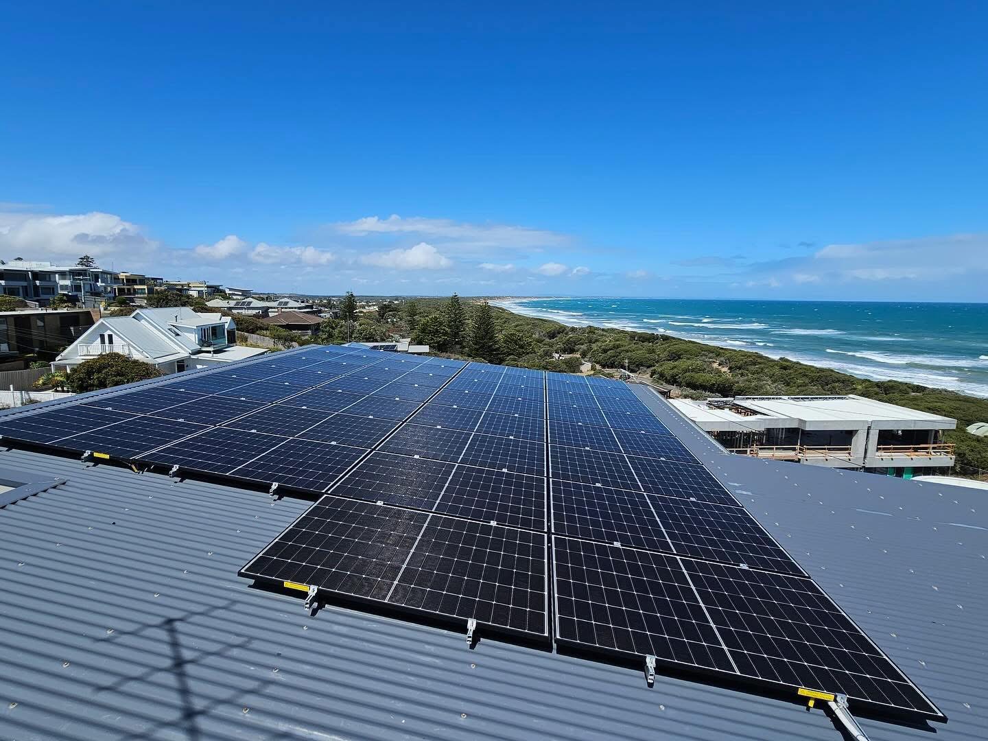 Solar panel array on grey colorbond roof with Tasmanian coastline behind